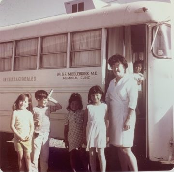 An Amigos Internacionales mobile medical clinic bus with four children and a clinic worker standing beside it